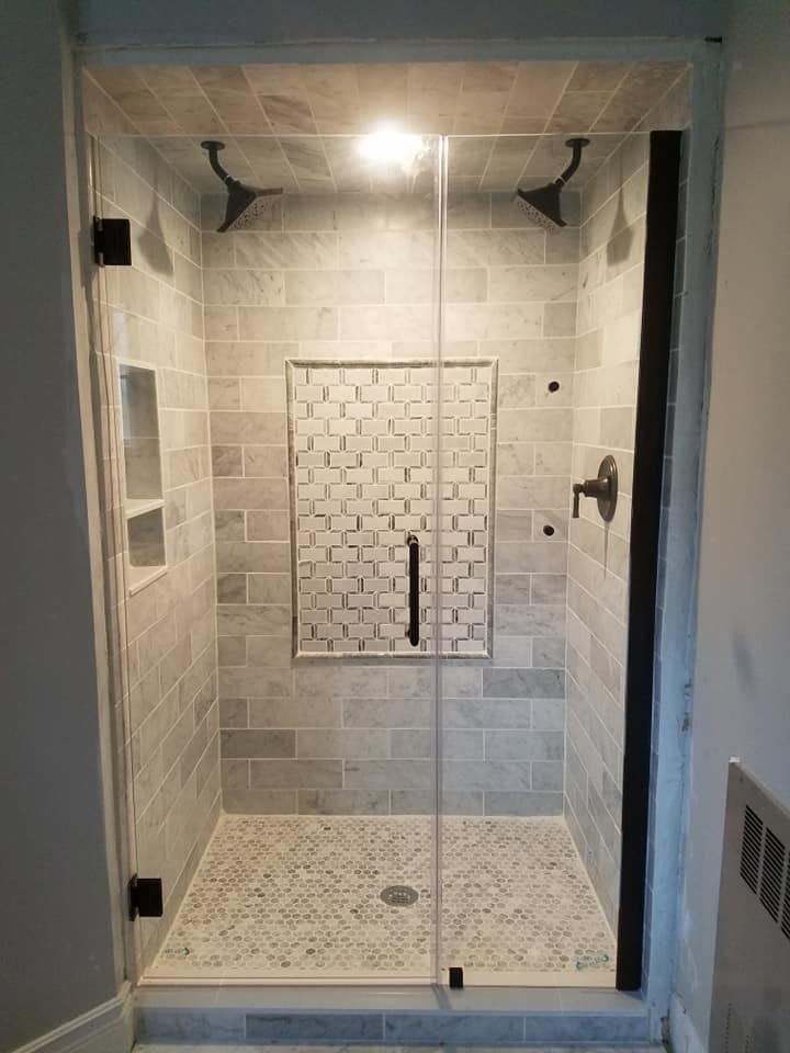 Elegant and timeless, Carrera Marble was used for the field for this shower in Falmouth, Maine. Marble mosaic was used for the detail the soap niche. The dark trim kit adds stark contrast and makes the shower quite striking behind the glass doors.